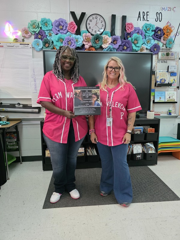 Two teachers wearing pink with sign.