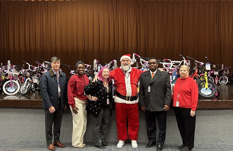 Six people standing in front of a stage of newly donated bicycles.