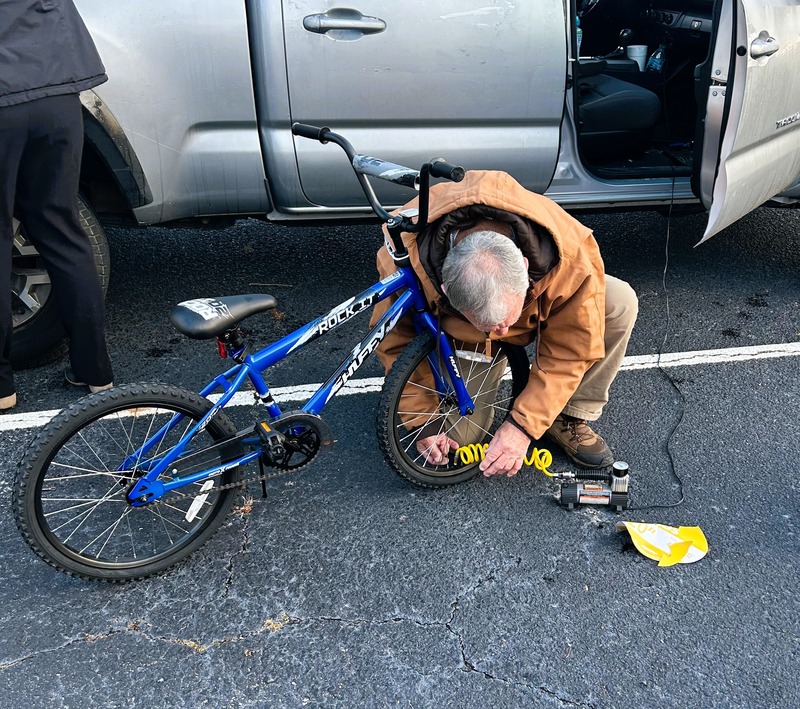 A man is pumping a bicycle tire by a silver truck.