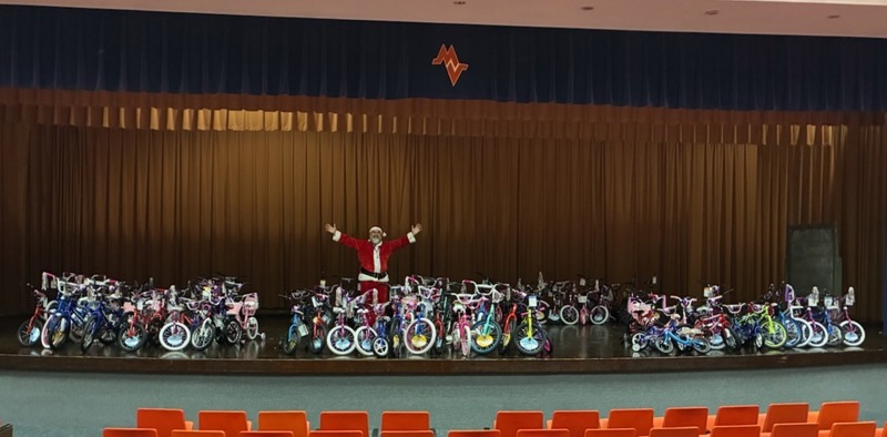 A man in a Santa suit showcasing bikes on a stage.