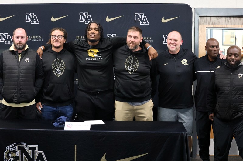 Group of coaches arm in arm with football player.