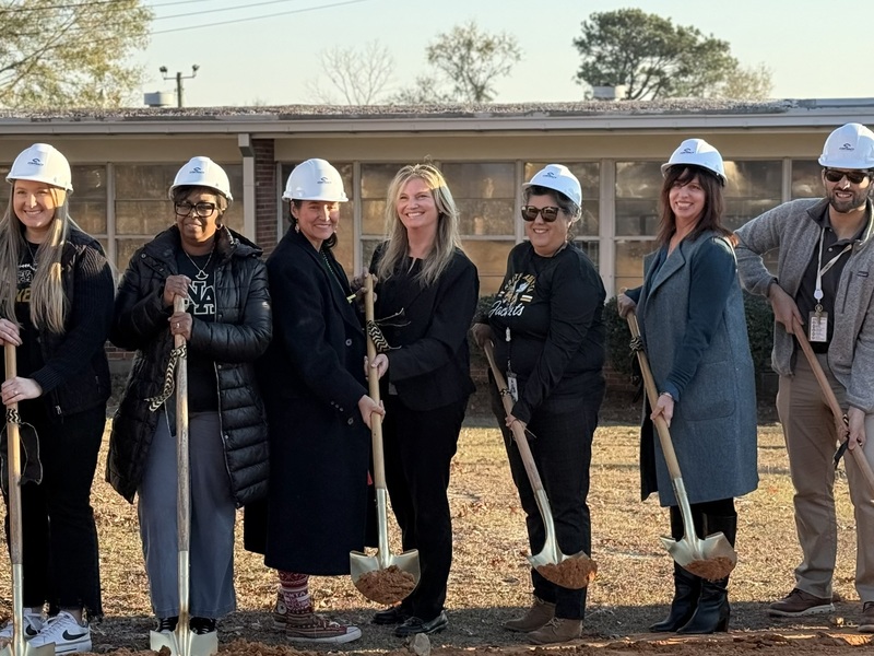 Principal with staff holding shovels, wearing hard hats, ready to break ground.