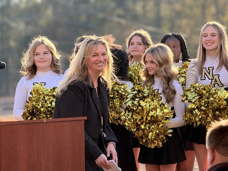 Principal wraps up a speech smiling with cheerleaders behind her.