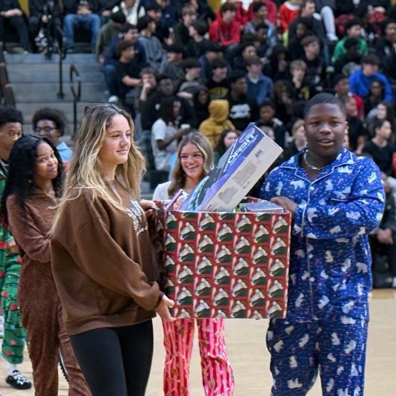 Two girls walking while carrying a large box filled wrapped donated gifts. 