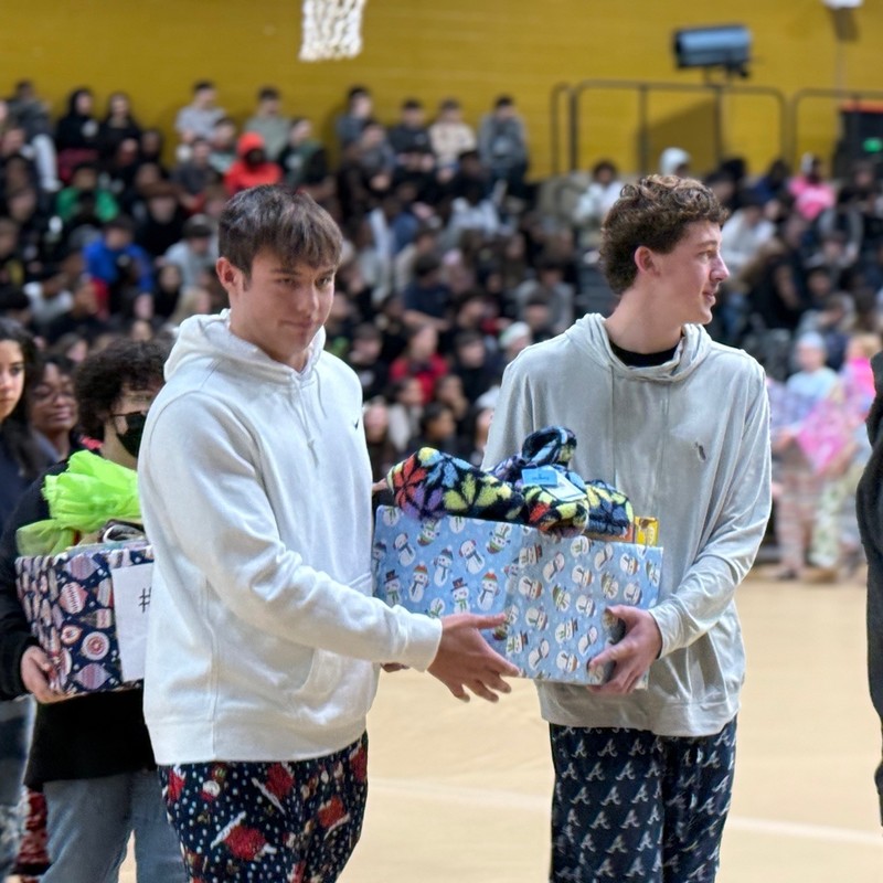 students carrying wrapped gifts to place around a tree.