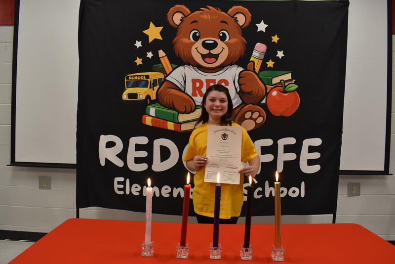 Student standing behind candles holding certificate.