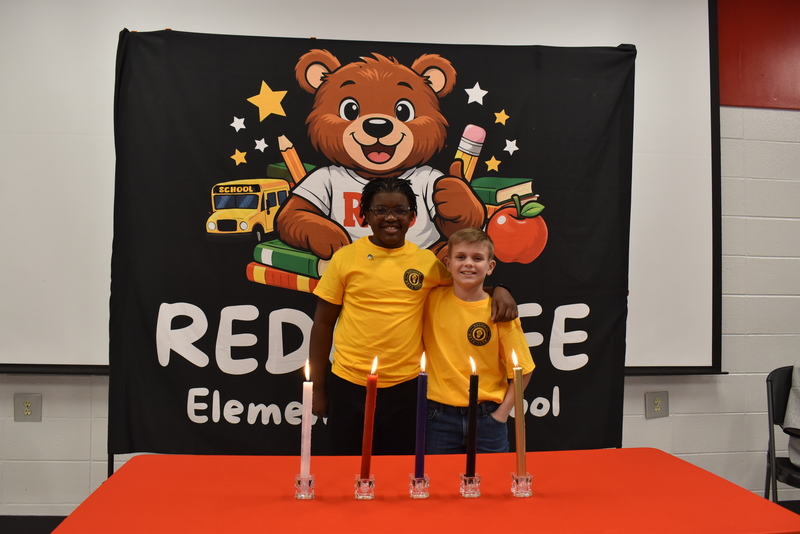 Two boys standing behind candles.