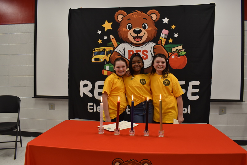 Three girls standing behind candles.