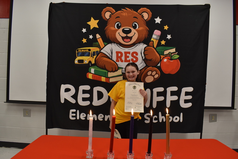 Student standing behind candles holding certificate.