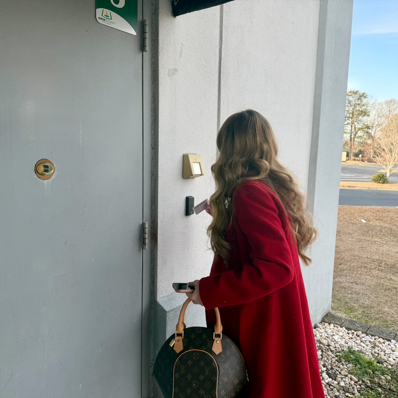 Student wearing a red coat letting themselves into a building with their badge. 