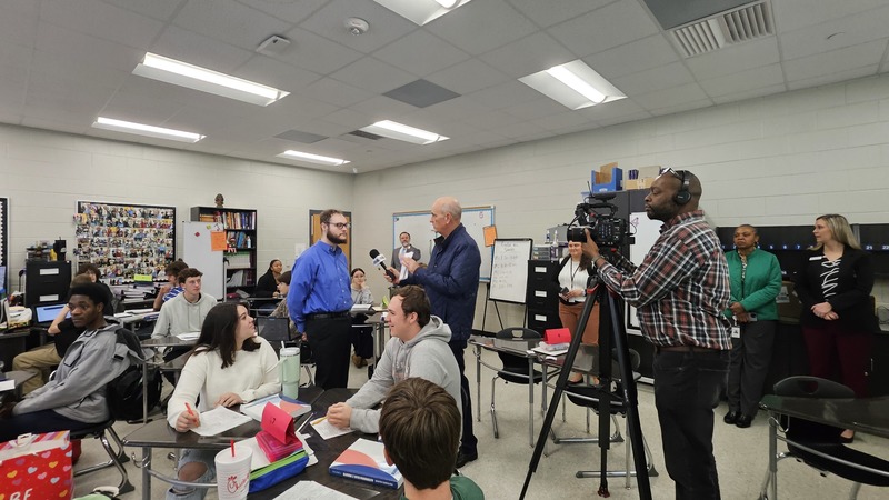Teacher being interviewed with camera crew and students.