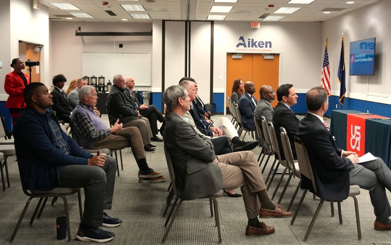 Political and education leaders listen during memorandum signing.