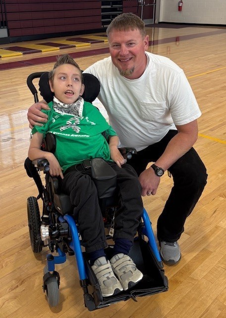 A male teacher kneels next to a boy in a wheelchair.