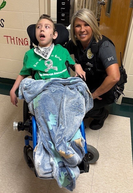 A resource officer kneels next to a boy in a wheelchair.