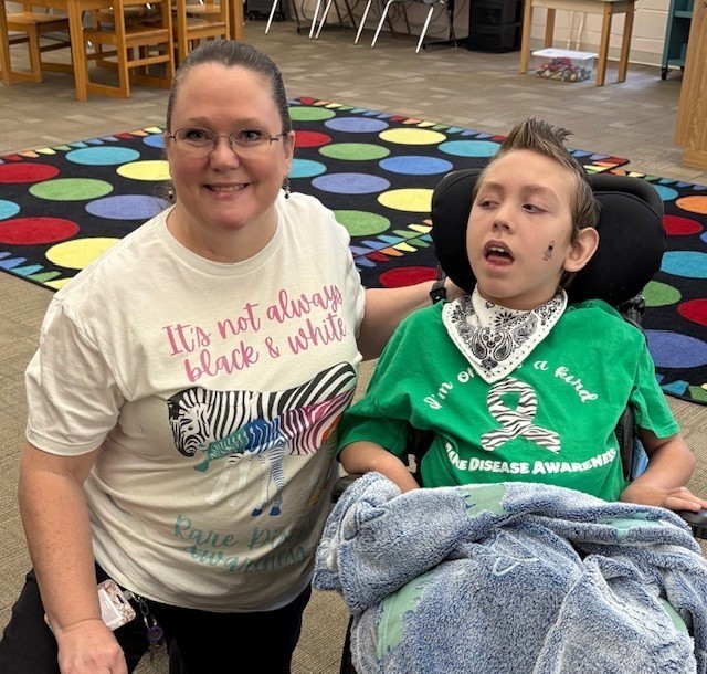 A teacher kneels next to a boy in a wheelchair.