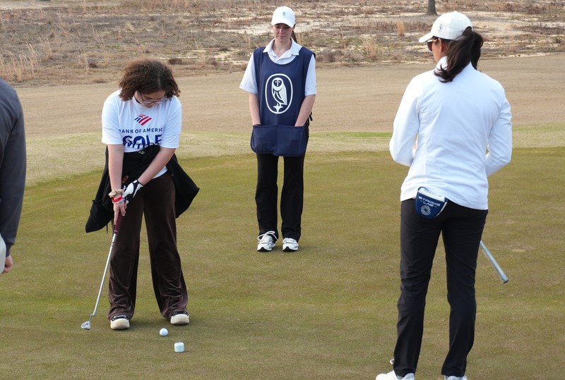 Instructors watch student putt on the green.