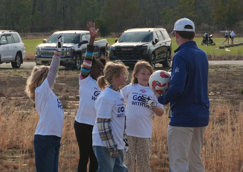 Students gather around soccer ball and instructor during foot golf drill.
