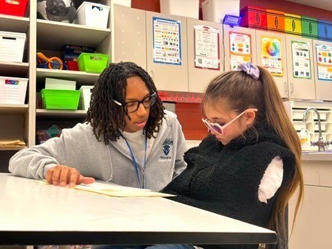 Howard student in classroom helping student. 