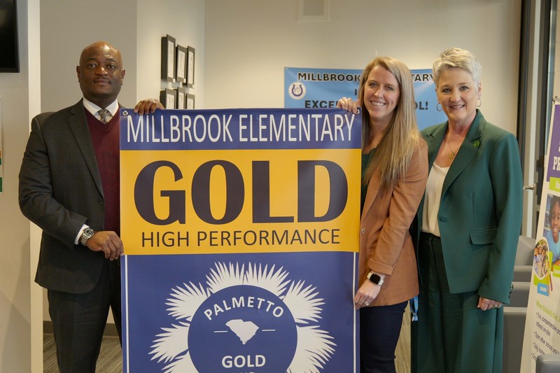 Millbrook principal stands with district leadership and banner.