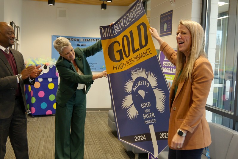 Gold banner is rolled out with three people looking at it.