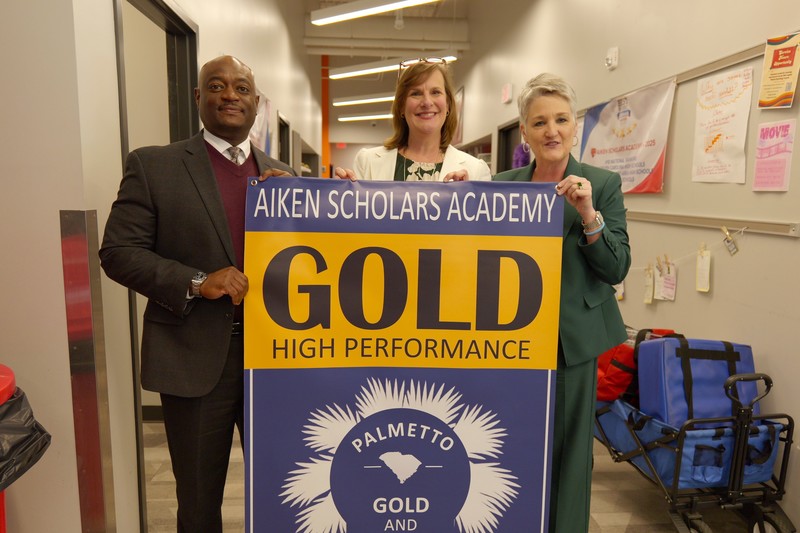 ASA principal Martha Messick stands with district leadership and gold performance banner.