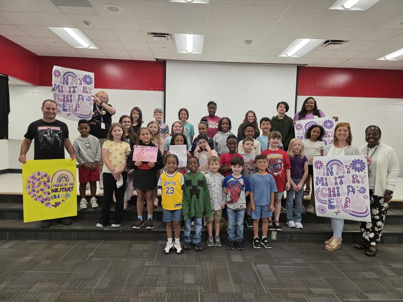 Students and staff standing on stage holding signs for the military child parade.