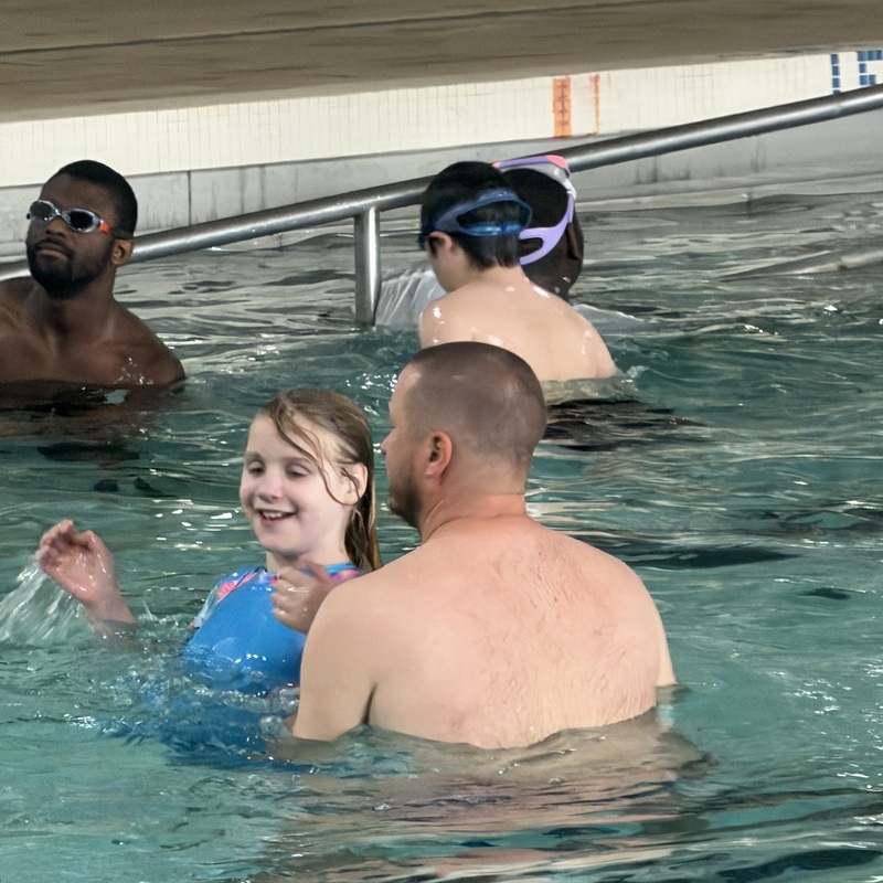 An image of swimming pool with children and adults.