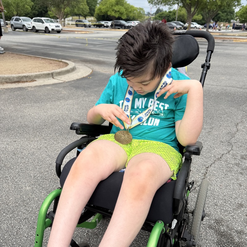 A male student in a wheelchair holds a medal.