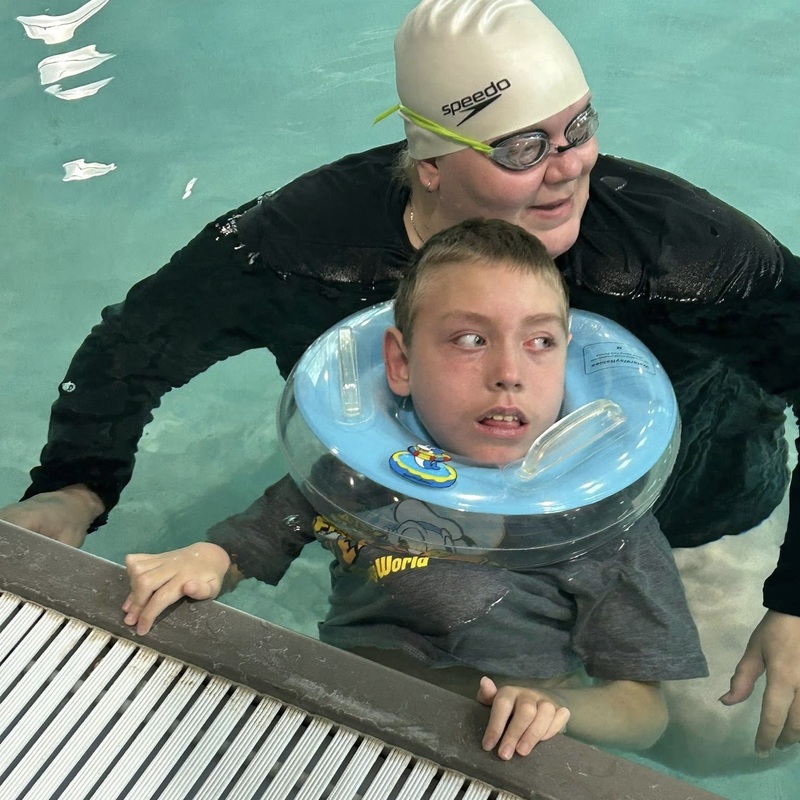 An adult and a boy are in a swimming pool.