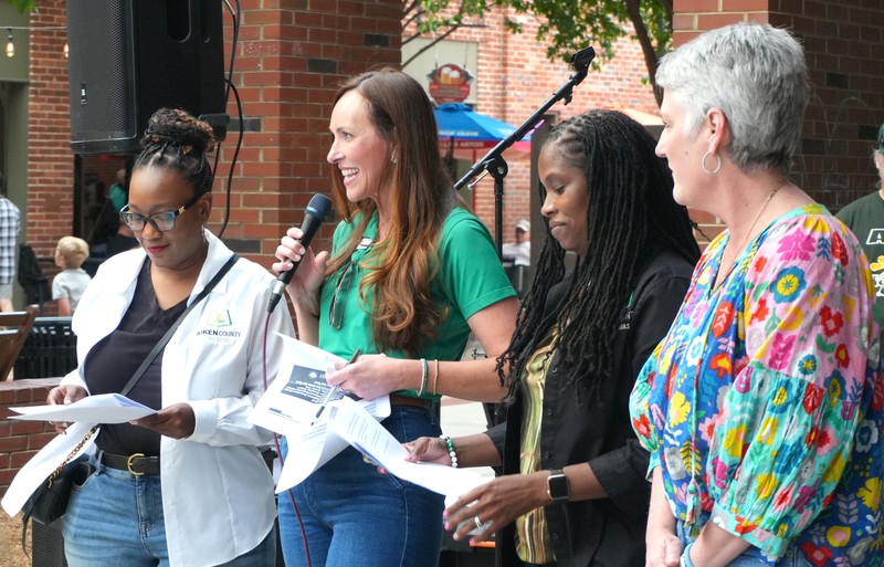 Four women announce information at an event.