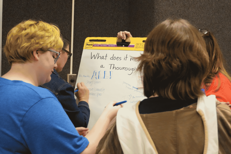 Students and community members writing on paper titled what does it mean to be a thoroughbred?