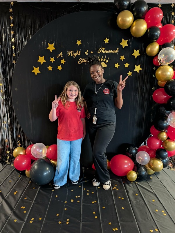 Student and staff posing in front of black backdrop that says "Night of a Thousand Stars".