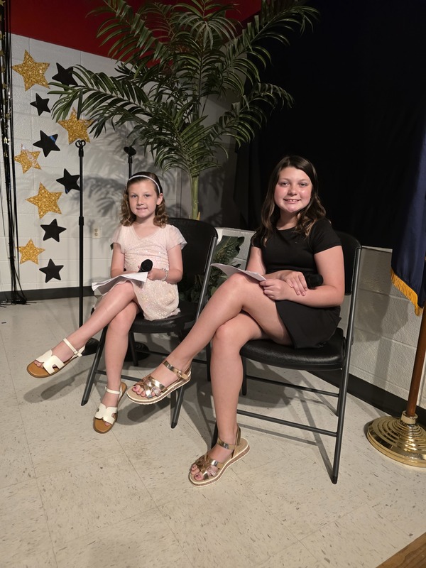 Two girls sitting on stage.