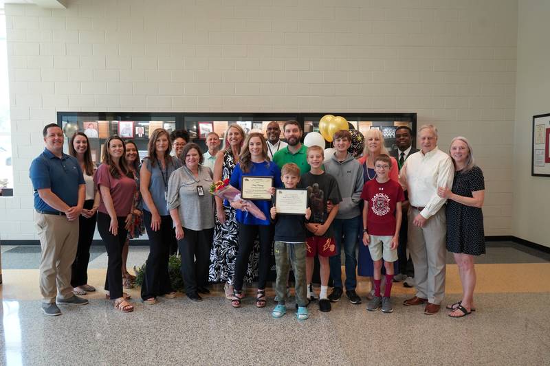 Group of Educators and award winner holding plaques with family in school lobby.