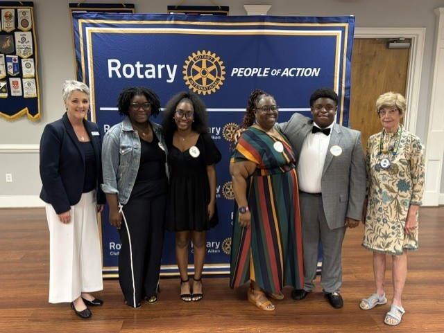 Community leaders and students pose together in front of a Rotary Club of Aiken banner.