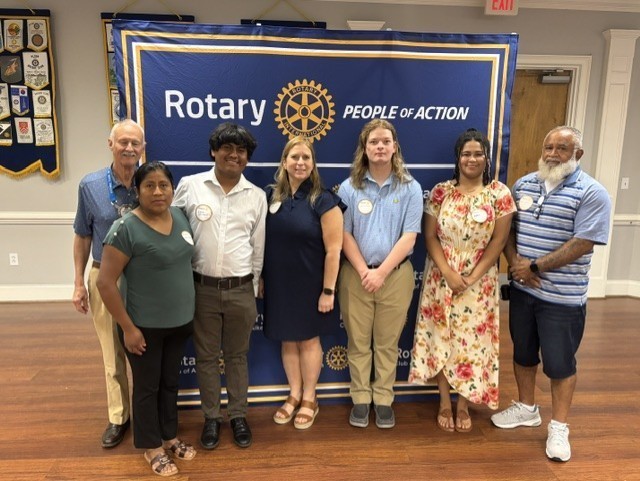 Community leaders and students pose together in front of a Rotary Club of Aiken banner.