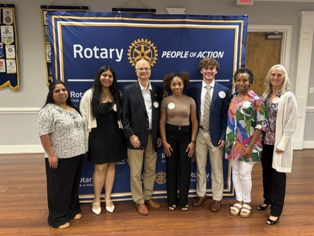 Community leaders and students pose together in front of a Rotary Club of Aiken banner.