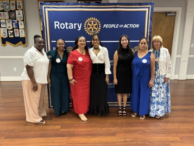 Community leaders and students pose together in front of a Rotary Club of Aiken banner.