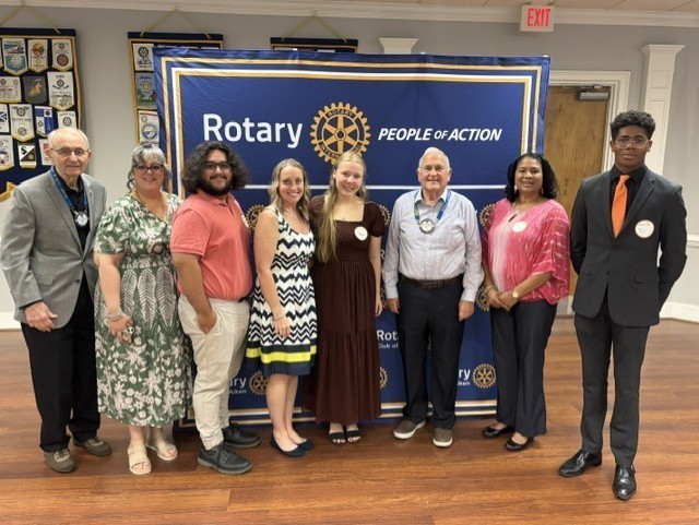 Community leaders and students pose together in front of a Rotary Club of Aiken banner.
