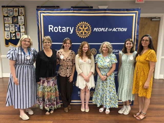 Community leaders and students pose together in front of a Rotary Club of Aiken banner.