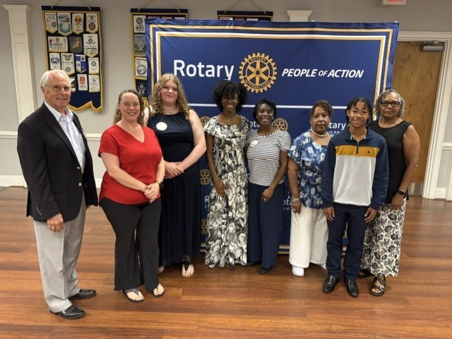 Community leaders and students pose together in front of a Rotary Club of Aiken banner.