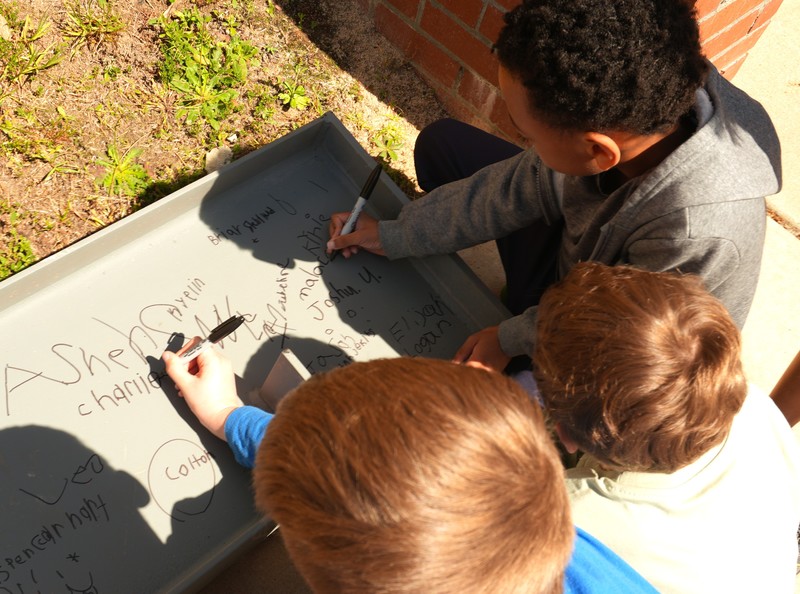 Two students sign their name on a beam.