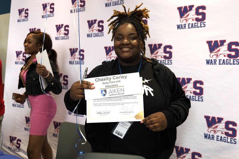 Student poses with nameplate and certificate.