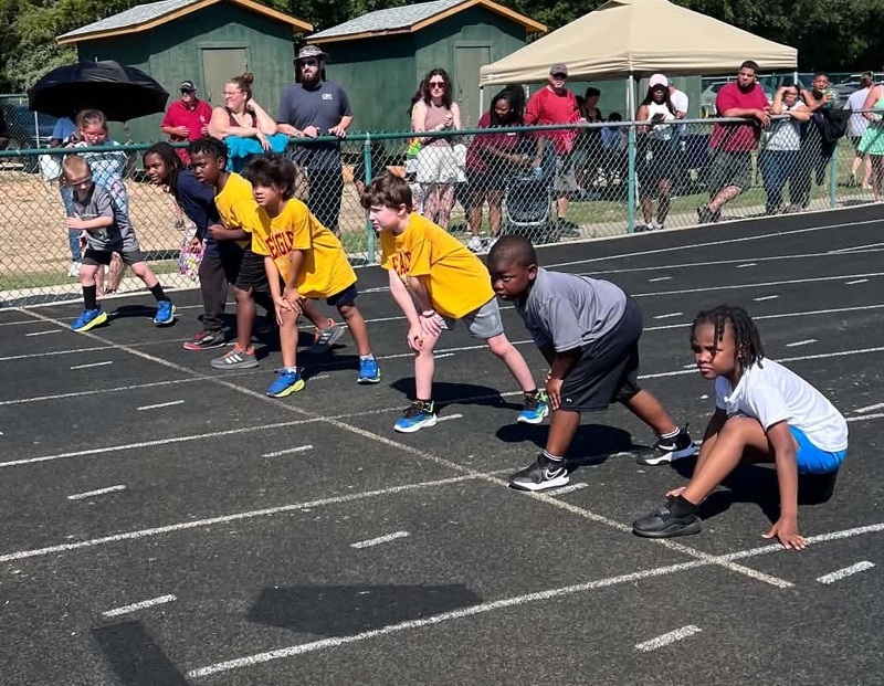 A picture of seven boys on the starting line of a race with onlookers in the background.