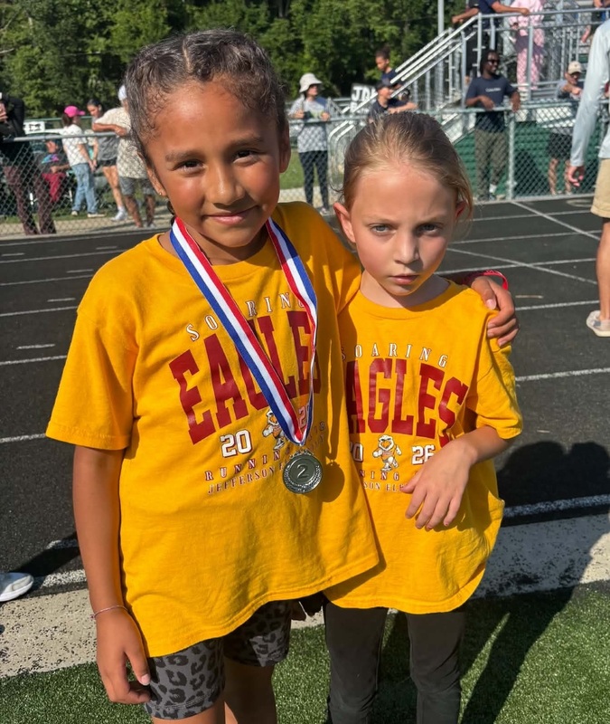 One girl wearing a medal stands with her arm around a teammate.
