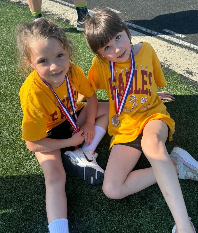 Two girls wearing medals sit side by side.