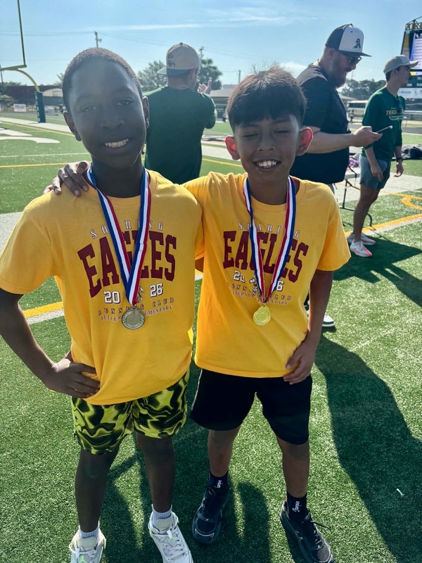 Two boys wearing medals stand arm in arm.