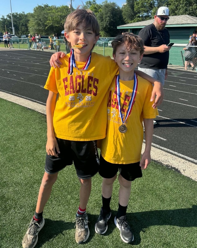 Two boys wearing medals stand arm in arm.