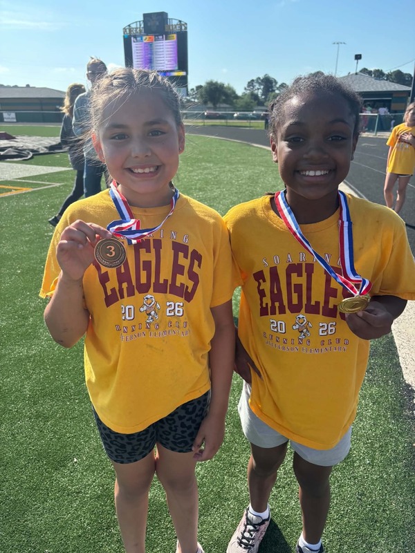 Two girls stand showing their medals they won.