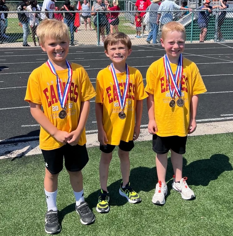 Three boys wearing medals stand side-by-side.